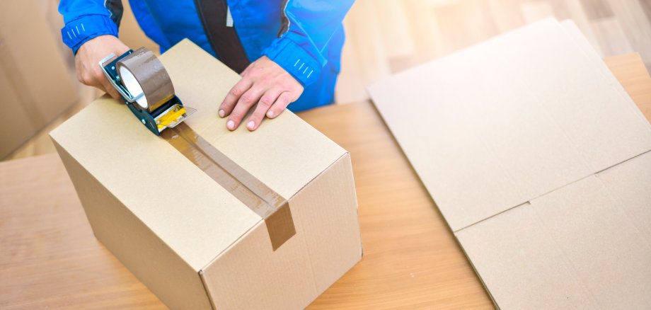 Worker hands holding packing machine and sealing cardboard or paper boxes 