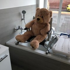 Teddybär sitzt auf einem Badewannensitz in der Badewanne