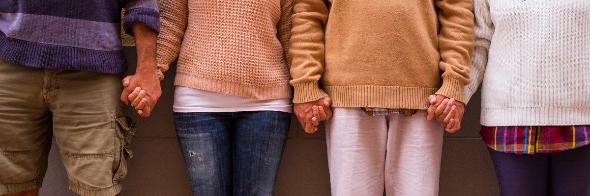 four people together holding their hands together in a community with a wall at the background - adults unity after covid19 